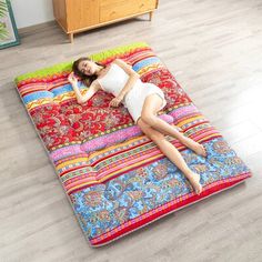 a woman laying on top of a multicolored blanket in the middle of a room