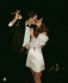 two people standing next to each other holding wine glasses in their hands and kissing on the lips