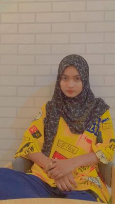 a young woman sitting in a chair wearing a yellow shirt and black scarf with stickers on it