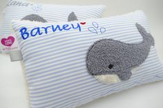 two blue and white striped pillows with an embroidered whale on the front one has a name written on it