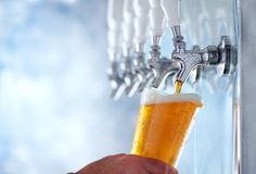 a person is holding a glass of beer in front of a row of faucets