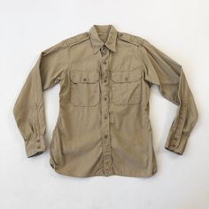 "1950's Marines khaki long sleeve shirt has a buttoned chest pockets, epaulettes, and a button front and cuff. Condition Structurally good. Has yellowish discoloration across the back, on both sleeves and around the front hem. Measurements Chest 40\" Waist 36\" Shoulder 15\" Sleeve length 25\" Length 27.5\" front, 30.5\" back. Best for a size small." Khaki Button-up Shirt With Button Cuffs, Classic Khaki Shirt With Pockets, Khaki Long Sleeve Shirt With Flap Pockets, Classic Khaki Shirt With Button Cuffs, Khaki Shirt With Spread Collar And Buttons, Khaki Shirt With Buttons And Spread Collar, Classic Long Sleeve Khaki Shirt, Khaki Long Sleeve Shirt With Placket, Classic Khaki Shirt With Buttons