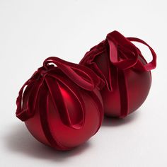 two shiny red ornaments with ribbons tied around them on a white surface, one ornament shaped like a ball