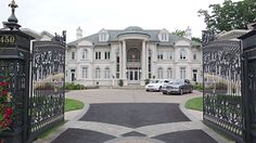 two cars are parked in front of a large house with an iron gate that leads to the driveway