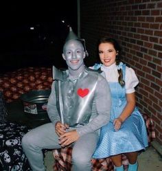 two people dressed up as wizard and tinkerbells sitting on a bench in front of a brick wall