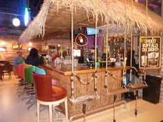 a tiki bar with stools and chairs around the bar area, in a restaurant