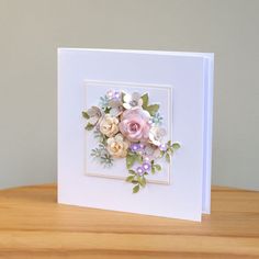 a card with flowers on it sitting on top of a wooden table in front of a gray wall