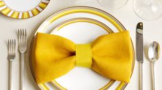 a yellow bow tie sits on top of a dinner table set with silverware and wine glasses