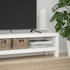 a flat screen tv sitting on top of a white shelf next to a potted plant