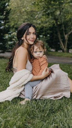 a woman sitting in the grass holding a baby