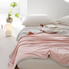 a bed with pink sheets and pillows on top of it next to a potted plant