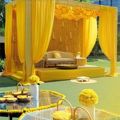 an outdoor seating area with yellow drapes and flowers