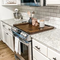 a kitchen with white cabinets and marble counter tops, stainless steel appliances and wooden cutting board