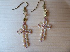 a pair of earrings with pearls and a cross hanging from the earwires on a wooden surface