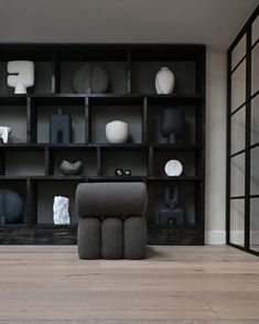 a chair sitting in front of a book shelf filled with vases