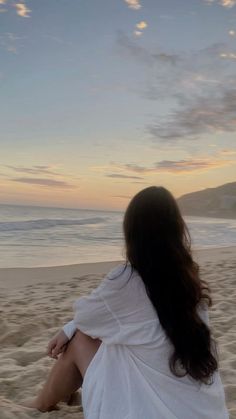 a woman sitting on top of a sandy beach next to the ocean under a cloudy sky