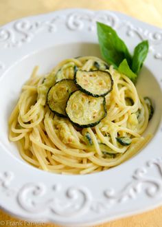 a white plate topped with pasta and zucchini on top of a wooden table