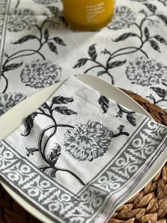 a table topped with plates and napkins covered in black and white flowers next to a jar of orange juice