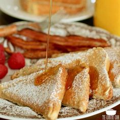 powdered sugar being drizzled onto pastries on a plate with raspberries