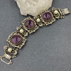 Vintage Victorian Revival Book Chain Bracelet With A Wonderful “Old Gold” Plating. The Large Purple Glass Cabochons Show A Mottled Effect And Are Mounted On Large Ornate Panels. Smaller Elongated Panels Are Adorned With Glowing Faux Pearls. Tight And Secure Fold Over Clasp. Measures 7 By 1 1/4” And Is Unsigned. Glass Book, Victorian Revival, Vintage Victorian, Purple Glass, Fold Over, Purple Gold, Gold Plating, Womens Jewelry Bracelets, Chain Bracelet