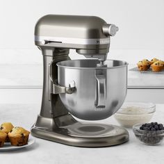 a silver mixer sitting on top of a counter next to blueberries and muffins