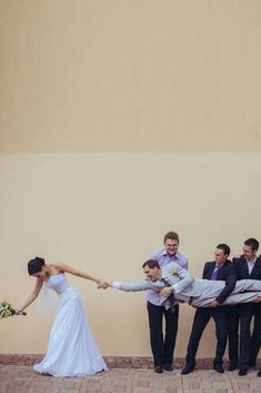 a bride and groom holding hands with their wedding party in front of a tan wall