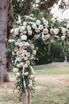 a wooden cross decorated with flowers and greenery in front of a large oak tree