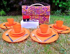 an orange table set with matching plates and cups on the grass in front of a purse