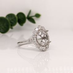 a white gold ring with diamonds and leaves on the side, sitting next to a green plant