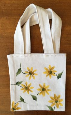 "This is a hand painted white canvas tote. The canvas is soft and flexible. The front of the tote is painted, The back and handles were not painted. The handles are made of the same type of material as the tote. The tote measures: The tote bag is 5.5\" tall x 5.5\" wide (excluding the handles). The total height of the tote - with the handles - is approximately 9.5\". I hand painted the front of the tote with scattered daisies - there are 6 daisies in all. I used fabric paint which is hand washable. The daisies are painted with bright yellow and yellow ochre.  The stems and leaves are painted in two shades of green. The tote is perfect for a small gift, party favor, or personal carry all. Please note: if you purchase 2 or more items on the same day from my shop, I will combine the packaging Hand Painted White Cotton Canvas Bag, Hand Painted White Canvas Tote Bag, White Hand Painted Canvas Tote Bag, Hand Painted White Canvas Bag, Hand-painted White Canvas Bag, White Hand Painted Rectangular Bag, White Hand Painted Canvas Bag, Everyday White Hand Painted Canvas Bag, White Rectangular Hand Painted Bag