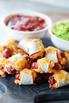 hot dogs stuffed with cheese and toppings on a cutting board next to guacamole