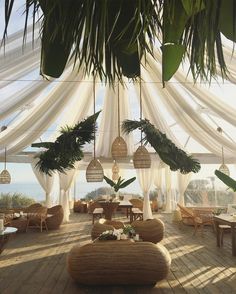 an outdoor dining area with wicker furniture and white drapes on the ceiling, surrounded by greenery