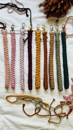 six different colored cords are lined up on a white sheet with pine cones in the background