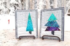 two small quilted christmas trees sitting on top of snow covered ground