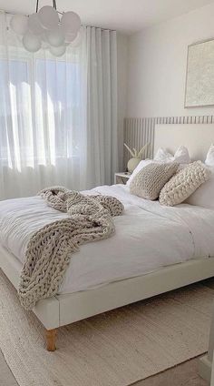 a white bed sitting in a bedroom next to a window covered in blankets and pillows