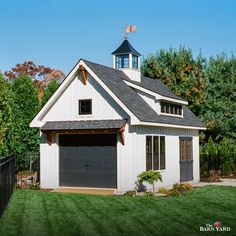 a garage with a steeple on the top and a dormer above it, in front of a fenced yard