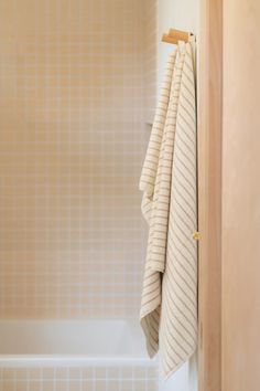 towels hanging on the side of a bathtub next to a wooden door in a bathroom