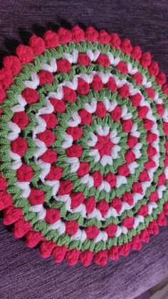 a crocheted red and green placemat on a purple blanket with white circles