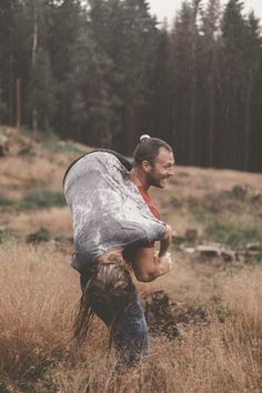 a man carrying something in his back while walking through tall grass with trees in the background