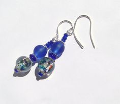 These earrings are made with gorgeous vintage foil glass beads with blues, greens, aquas, and amber speckles that have been combined with deep blue matte glass beads and accented with glittery royal blue seed beads. Hanging Length: 2 inches. Ear wires: silver plated surgical steel. Blue Round Beaded Earrings With Spacer Beads, Blue Earrings With Spacer Beads For Gift, Nickel-free Blue Recycled Glass Earrings, Blue Nickel-free Recycled Glass Earrings, Blue Recycled Glass Nickel-free Earrings, Blue Czech Glass Beaded Earrings With Dangling Beads, Blue Czech Glass Beaded Earrings, Blue Recycled Glass Dangle Earrings, Blue Glass Earrings With Dangling Beads