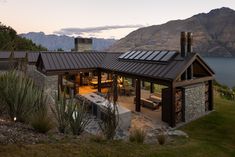 a house with a metal roof next to a body of water and mountains in the background