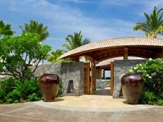 two large brown vases sitting in front of a stone building with palm trees around it