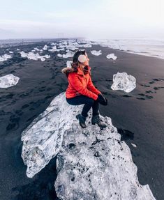 a woman in an orange jacket sitting on top of some ice flakes and looking at the camera