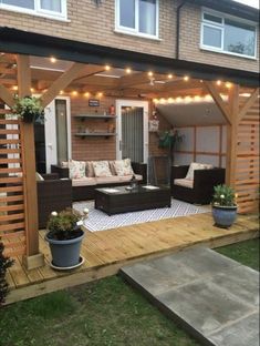 an outdoor living area with couches and lights on the roof, in front of a house