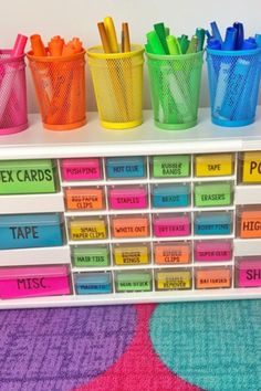 colorful plastic cups and markers are arranged on a white shelf with multicolored labels