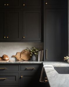 a kitchen with black cabinets and marble counter tops, along with wooden cutting boards on the counters