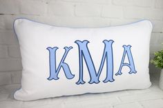 a white pillow with blue trim and the word kma on it, next to a potted plant