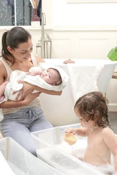 a woman holding a baby in a bathtub with two other babies around her,