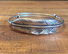 "This listing is for one silver stainless steel feather cuff. This cuff is adjustable from 6 1/2\" up to 9 1/2\". It is 1/2\" wide and 9 1/2\" long. It is bendable but sturdy with an overlapping adjustable band. Could fit a man's wrist if expanded. This bracelet contains copper. This should only be cleaned with soap and water and a clean soft cloth. Any lotions or perfumes can change the color of the bracelet. Any rubbing or excessive cleaning may damage the finish." Adjustable Antique Silver Cuff Bangle, Casual Silver Bangle Cuff Bracelet, Adjustable Antique Silver Metal Cuff Bracelet, Adjustable Antique Silver Sterling Silver Cuff Bracelet, Casual Silver Bracelet With Adjustable Band, Feather Cuff Bracelet, Feather Cuff, Ladies Bracelet, Silver Cuff Bracelet