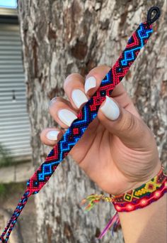 a woman holding up a colorful bracelet next to a tree